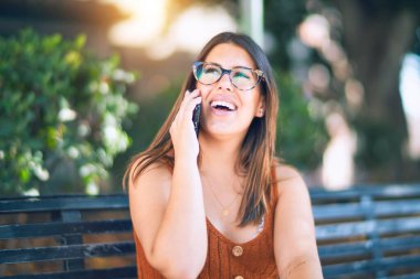 Mutlu ve kendinden emin gülümseyen genç ve güzel bir kadın. Yüzünde bir gülümsemeyle şehirde akıllı telefon başında konuşmak.