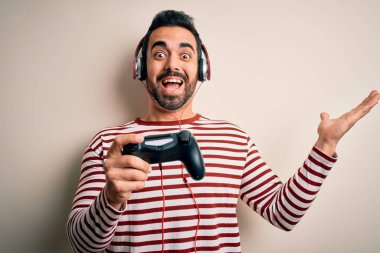 Sakallı, video oyunu oynayan yakışıklı oyuncu joystick ve kulaklıkla çok mutlu ve heyecanlı, kazanan yüz ifadesi zaferi büyük bir gülümsemeyle kutluyor ve ellerini kaldırıyor.