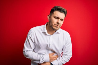 Mavi gözlü genç bir iş adamı kırmızı izole edilmiş arka plan üzerinde duruyor. Midesinde hazımsızlık, acı verici bir hastalık var. Ache kavramı.
