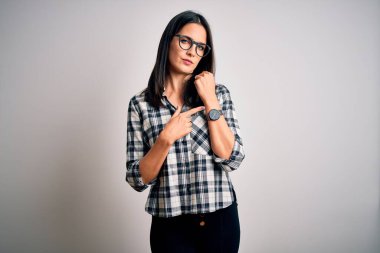 Mavi gözlü, sıradan gömlekli, beyaz arka planda gözlüklü genç esmer kadın. Aceleyle saati, sabırsızlığı ve rahat bir ifadeyle kameraya bakıyor.