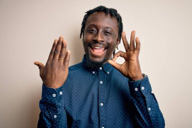 Genç Afrikalı Amerikalı adam beyaz arka planda altın evlilik yüzüğü gösteriyor. Parmaklarıyla tamam işareti yapıyor. Mükemmel bir sembol.