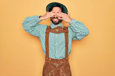 Almanya festivali için geleneksel Alman Ekim Festivali kıyafeti giyen yakışıklı genç adam neşeli ve komik gülümseyerek gözlerini kapatıyor. Kör kavram.