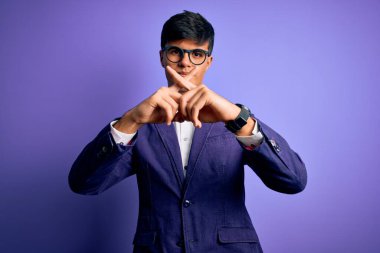 Ceket ve gözlük takan yakışıklı genç bir iş adamı mor arka planda reddedilme ifadesini olumsuz işaret yaparak umuyor.