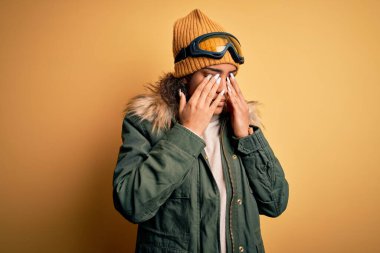 Genç Afro-Amerikan kayakçı kız kar sporu kıyafetleri ve kayak gözlüğü takıyor yorgunluk ve baş ağrısı için gözlerini ovuşturuyor uykulu ve yorgun bir ifade takınıyor. Görüş sorunu