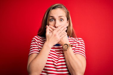 İzole edilmiş kırmızı arka plan üzerine sıradan çizgili tişört giyen genç, güzel sarışın kadın yanlışlıkla ağızlarını kapatarak şok etti. Gizli konsept.
