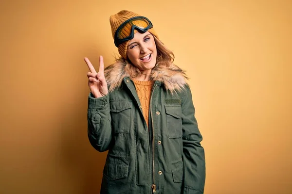 中年漂亮的金发滑雪者女人穿着雪地运动鞋和滑雪护目镜 高兴地微笑着 用手指在镜头前眨眼示意胜利 第二点 — 图库照片
