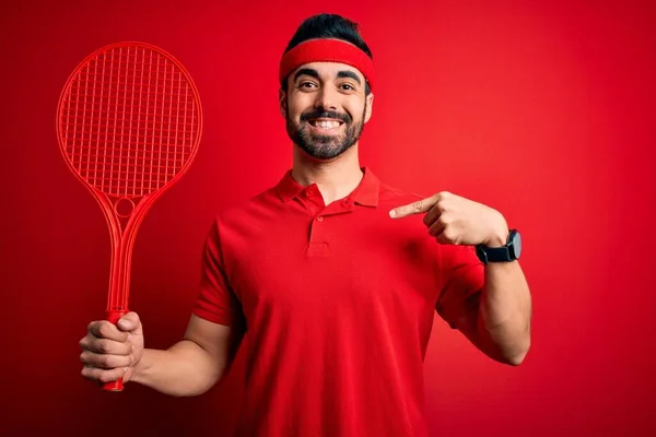 若いですハンサムなスポーツマンとともにひげ再生テニス使用ラケット以上赤背景とともに驚き顔指差し指に彼自身 — ストック写真