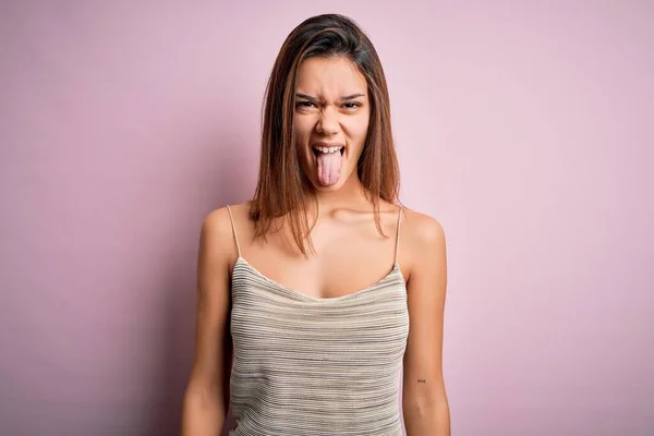 年轻美丽的黑发姑娘穿着休闲的条纹T恤 披着孤立的粉色背景 带着滑稽的表情伸出舌头 情感概念 — 图库照片