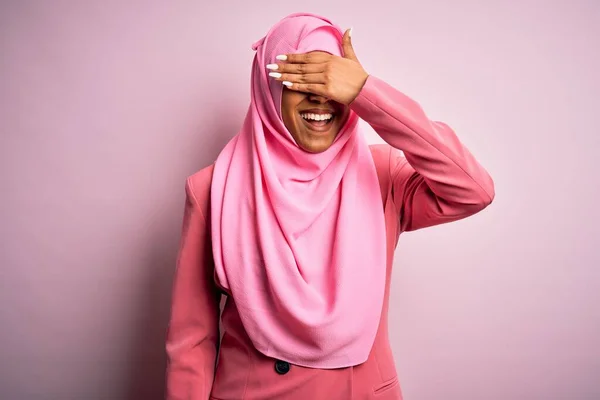 孤立したピンクの背景にイスラム教徒のヒジャーブを身に着けている若いアフリカ系アメリカ人のアフロ女性は笑顔で 驚きのために目を覆う顔で笑っています ブラインドコンセプト — ストック写真