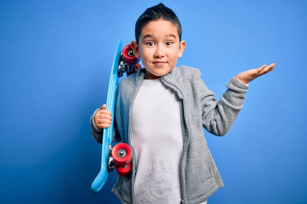 小男孩滑板手抱着现代滑板在蓝色孤立的背景上 非常高兴 胜利的表情带着大大的微笑和举手庆祝胜利的胜利 — 图库照片