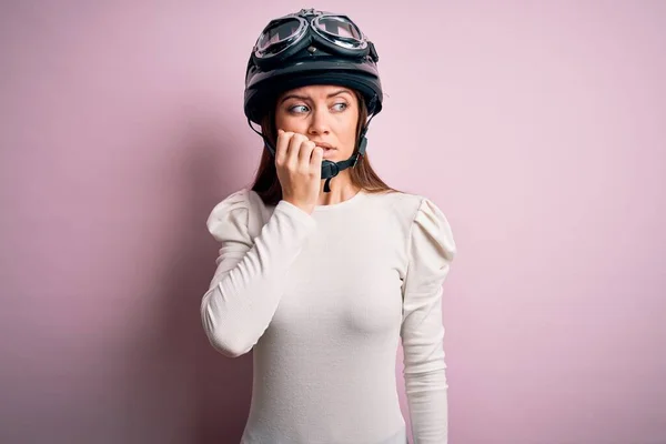 ピンクの背景に元のヘルメットを身に着けて青い目を持つ若い美しいオートバイの女性は 口の爪をかむ上で手でストレスと緊張を見て 不安の問題 — ストック写真