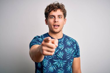 Tatilde, kıvırcık saçlı, yaz tişörtü giyen genç sarışın adam kameraya kızgın ve sinirli bir şekilde seni işaret ediyor.