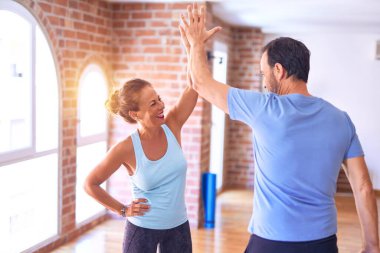 Orta yaşlı güzel sporcu çift mutlu gülümsüyor. Yüzünde gülümsemeyle spor salonunda beşlik çakıyor.