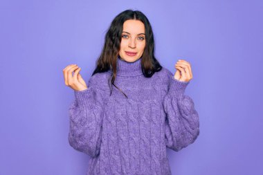 Balıkçı yaka kazak giyen genç güzel bir kadın mor arka planda duruyor. Elleriyle para hareketi yapıyor. Maaş ödemesi istiyor.