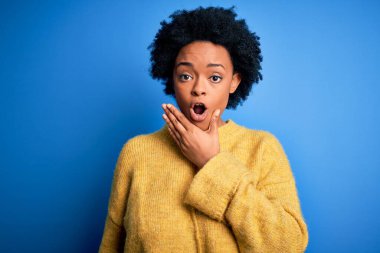 Sarı günlük kazak giyen kıvırcık saçlı, genç, Afro-Amerikan bir kadın. İnançsızlıktan, şaşkınlıktan ve elleri çenesinde olan şaşkınlıktan büyülenmiş görünüyor.