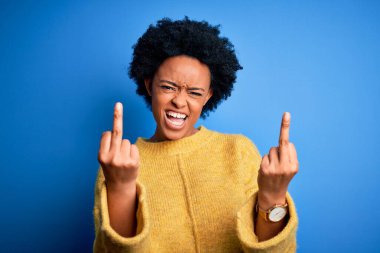 Young beautiful African American afro woman with curly hair wearing yellow casual sweater Showing middle finger doing fuck you bad expression, provocation and rude attitude. Screaming excited