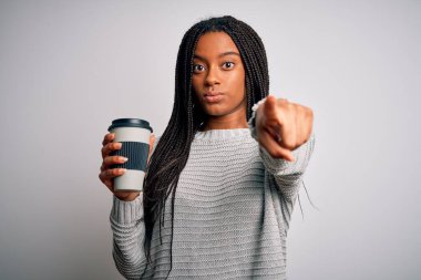 Genç Afrikalı Amerikalı bir kız izole edilmiş arka planda plastik bir fincanda kahve içerek kamerayı işaret ediyor ve sen, el işareti, ön taraftan pozitif ve kendinden emin bir jest.
