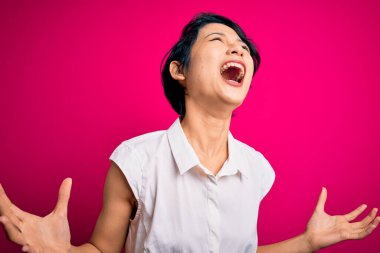 Genç, güzel Asyalı bir kız, sıradan bir yaz tişörtü giyip pembe arka planda dikiliyor. Deli deli deli bağırıyor ve agresif bir ifade ve kollarla bağırıyor. Hayal kırıklığı konsepti.