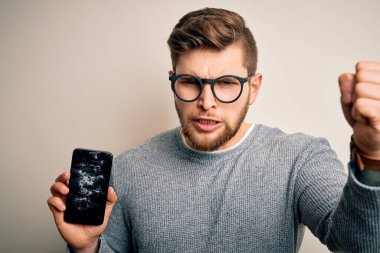 Sarışın, sakallı, mavi gözlü, gözlüklü, kırık akıllı telefon takan sinirli ve sinirli bir genç adam. Öfkeyle bağırıyor, çıldırıyor ve elini kaldırarak bağırıyor.