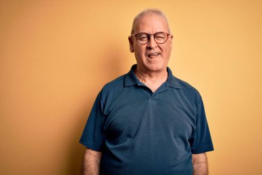 Orta yaşlı yakışıklı, beyaz tenli, sıradan polo giyen, sarı arka planda gözlüklü, seksi bir ifadeyle kameraya bakan, neşeli ve mutlu yüzlü bir adam..