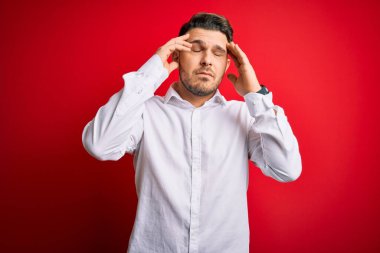 Mavi gözlü, zarif gömlekli genç bir iş adamı. Kırmızı izole edilmiş arka plan üzerinde duruyor. Baş ağrısı yüzünden. Migren ağrısı..