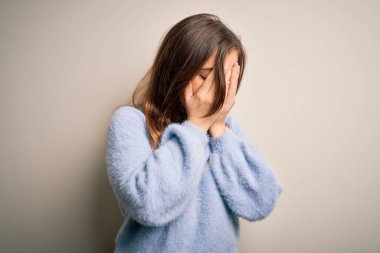 Kış süveteri giyen genç ve güzel bir kadın izole arka planda dikiliyor. Üzücü bir ifadeyle yüzünü ellerle kapatıyor ve ağlıyor. Depresyon kavramı.
