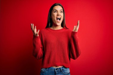 Güzel, genç, esmer bir kadın kırmızı bir arka planın üzerinde dikilmiş kızgın ve çılgın bir şekilde bağırıyor ve agresif bir ifade ve kollarla bağırıyor. Hayal kırıklığı konsepti.