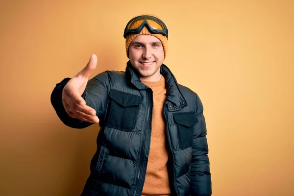 年轻英俊的高加索男子戴着帽子 外套和滑雪眼镜 在冬雪天气里友好地微笑 握手致意和欢迎 成功的业务 — 图库照片