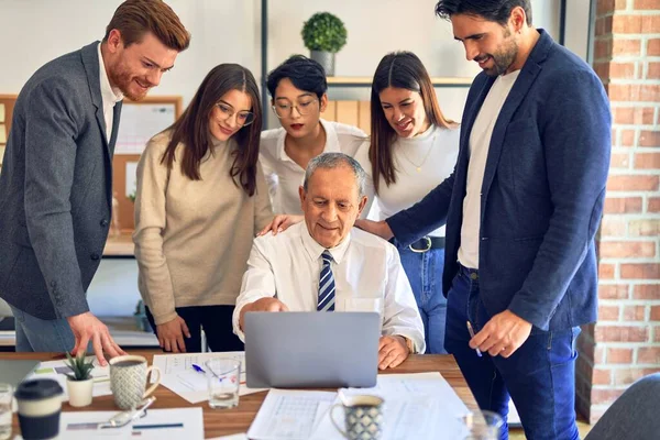 Group of business workers smiling happy and confident. One of them sitting and partners standing around. Working together with smile on face looking at the laptop at the office