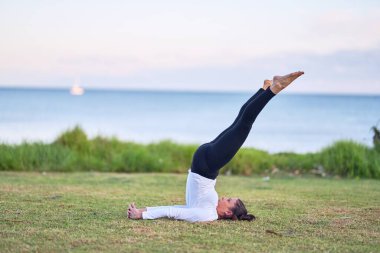 Young beautiful sportwoman practicing yoga. Coach teaching shoulder stand pose at park