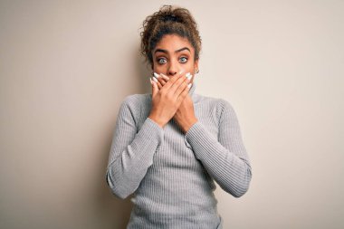 Güzel Afrikalı Amerikalı kız balıkçı yaka kazak giyiyor beyaz arka planda dikiliyor ağzı yanlışlıkla ellerle kapatıyor. Gizli konsept.