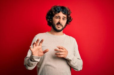 Sakallı, sıradan bir süveter giyen genç, tiksindirici ve tiksindirici bir yüz ifadesi takınan, tiksindirici bir yüz ifadesi takınan bir yakışıklı. Eller havada