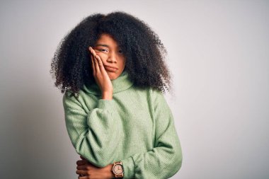 Afro saçlı, yeşil kazaklı, genç ve güzel Afro Amerikalı kadın kollarını kavuşturarak depresyondan sıkılmış ve yorgun göründüğünü düşünüyor..