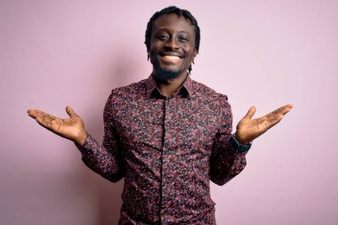 Genç, yakışıklı, Afro-Amerikalı bir adam pembe arka plan üzerinde dikilmiş gülümseyerek avuçlarını açıyor, sunuyor ve reklam karşılaştırması yapıyor ve dengeyi sağlıyor.