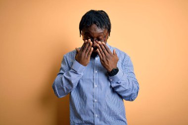 Sarı arka plan üzerine gömlek ve gözlük takan yakışıklı Afro-Amerikan erkeği yorgunluk ve baş ağrısı için gözlerini ovuşturuyor, uykulu ve yorgun bir ifade takındı. Görüş sorunu