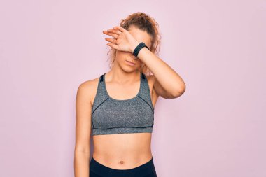 Genç, sarışın, mavi gözlü sporcu kadın spor kıyafetleri giyiyor, gözleri kollarıyla kapatıyor, ciddi ve üzgün görünüyor. Görme, saklama ve reddetme konsepti