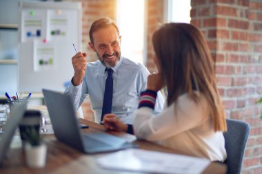 Mutlu ve kendinden emin gülümseyen iki orta yaşlı iş adamı. Ofiste dizüstü bilgisayarla gülümseyerek birlikte çalışıyoruz.