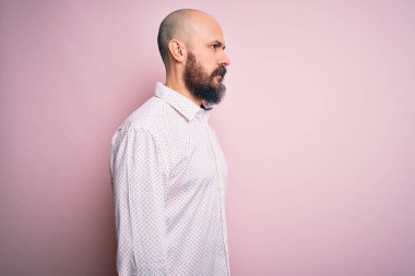 Sakallı, zarif tişörtlü yakışıklı, pembe arka planda, rahat bir görünüm takınan, kendine güvenen bir gülümsemesi olan kel bir adam..