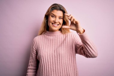 İzole edilmiş arka planda pembe süveter giyen genç, güzel, sarışın bir kadın gülümseyen ve kendine güvenen, el hareketi yapan, parmaklarıyla işaret eden ve kameraya bakan. Ölçü kavramı.