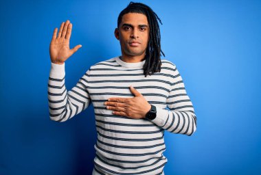 Genç, Afro-Amerikan Afrikalı, rastalı, sıradan çizgili bir kazak giyen, elleri göğsünde, elleri açık, sadakat yemini eden bir adam.