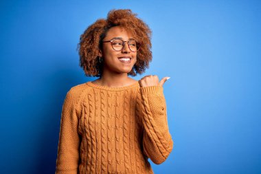 Kıvırcık saçlı, neşeli yüzüyle gülümseyen ve baş parmağıyla yüzünü gösteren güzel Afro-Amerikan kadın..