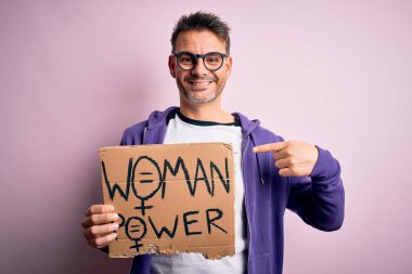 Genç ve yakışıklı bir adam kadın hakları için pankart istiyor. Elinde kadın gücü mesajı var. Yüzünde kendini gösteren sürpriz bir ifade var.
