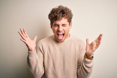 Sarışın, kıvırcık saçlı, beyaz arka plan üzerine gündelik süveter giyen genç ve yakışıklı bir adam, başarı için deli ve çılgın bir kutlama yapıyor. Kolları havada ve gözleri kapalı, heyecanla bağırıyor. Kazanan konsept