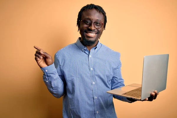 若いアフリカ系アメリカ人労働者の男作業ノートパソコンを使用して黄色の背景に立って非常に幸せなポインティングで手と指で側面 — ストック写真