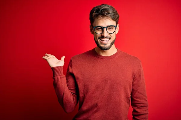 Sakallı Gözlüklü Süveterli Genç Adam Kırmızı Arka Planda Dikiliyor Gülümsüyor — Stok fotoğraf