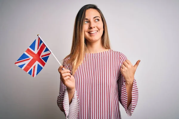 若いです美しいですブロンド女性とともに青い目を保持英国のフラグポインティングとととともに親指で側まで幸せな顔笑顔 — ストック写真