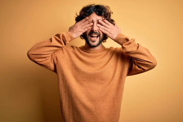 明るい笑顔と面白い手で目をカバー黄色の背景に立ってカジュアルなセーターを着てひげを持つ若いハンサムな男 ブラインドコンセプト — ストック写真