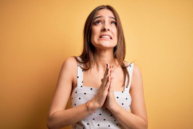 Sarı arka planda sıradan bir elbise giyen genç ve güzel esmer kadın elleri bağlı yalvarıyor ve dua ediyor. Yüzünde umut ifadesi var ve endişeli. Yalvarıyorum..