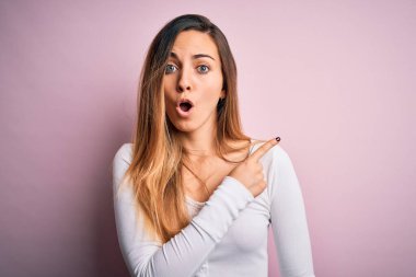 Pembe arka planda beyaz tişört giyen, mavi gözlü genç, güzel, sarışın bir kadın..