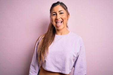 Pembe izole edilmiş arka plan üzerine kazak giyen genç ve güzel bir kadın komik bir ifadeyle dilini dışarı çıkartıyor. Duygu kavramı.